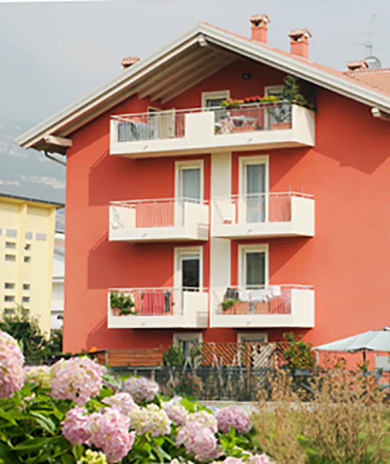 Residenza Alessandra a Rovereto: facciata rossa con balconi bianchi e ortensie in primo piano