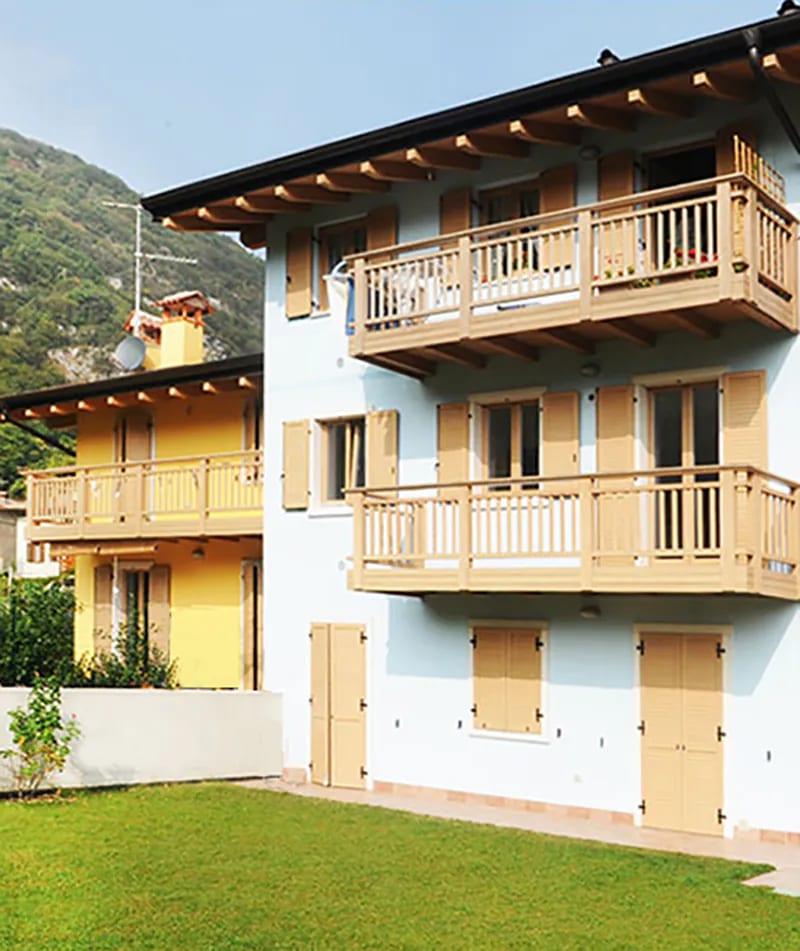 Residenza Amarilli: facciata chiara con balconi in legno e giardino, montagne sullo sfondo