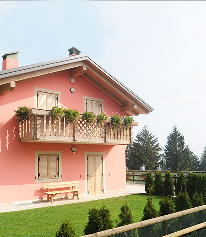 Residenza Gabriele: casa rosa con balcone in legno fiorito, panchina e prato
