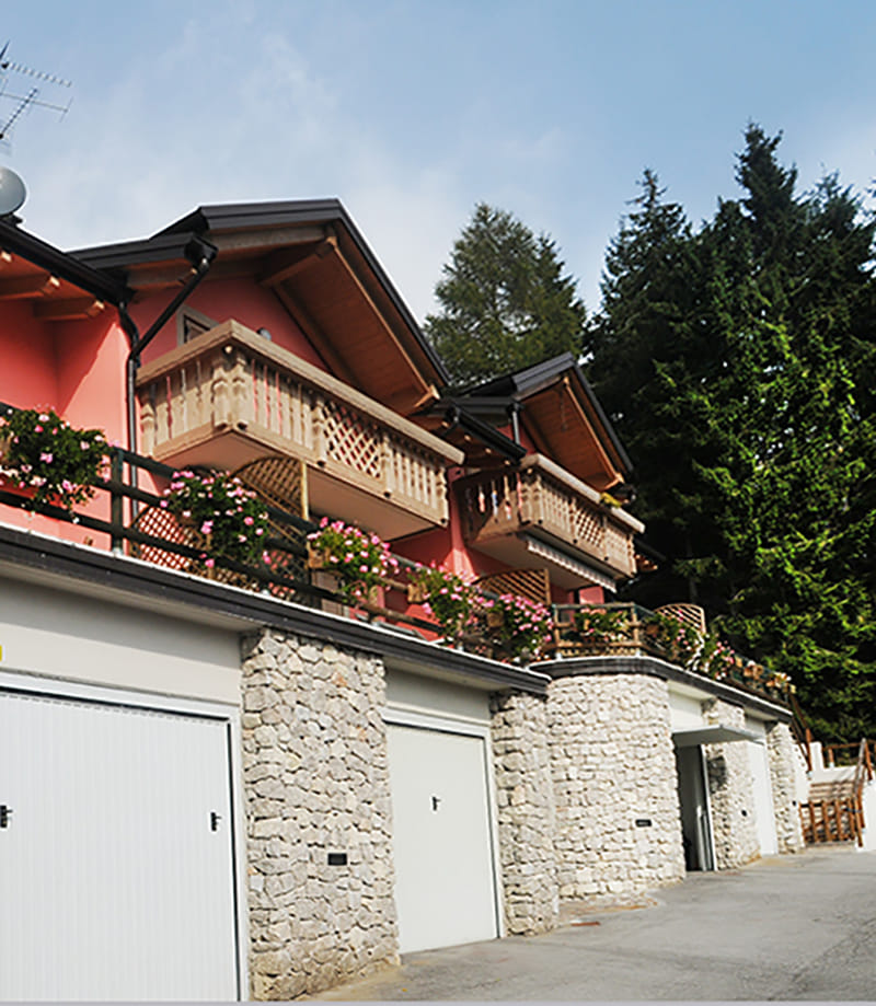 Residenza Gabriele: case con balconi in legno fioriti sopra garage con pilastri in pietra
