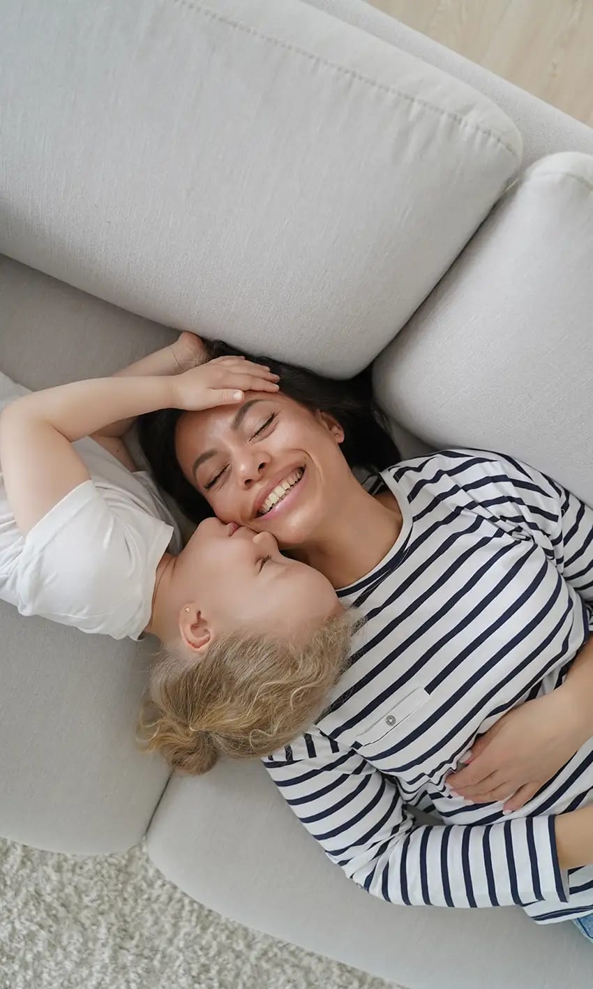 Donna e bambina sorridenti sdraiate su un divano chiaro